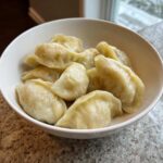 A white bowl filled with freshly steamed Traditional Chinese Dumplings resting on a speckled countertop.