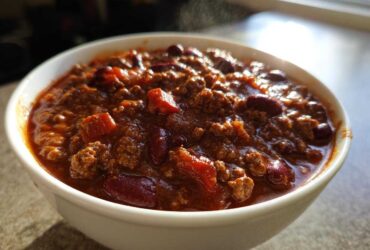 Close-up of a steaming white bowl filled with rich, hearty crockpot chili featuring ground meat and kidney beans.