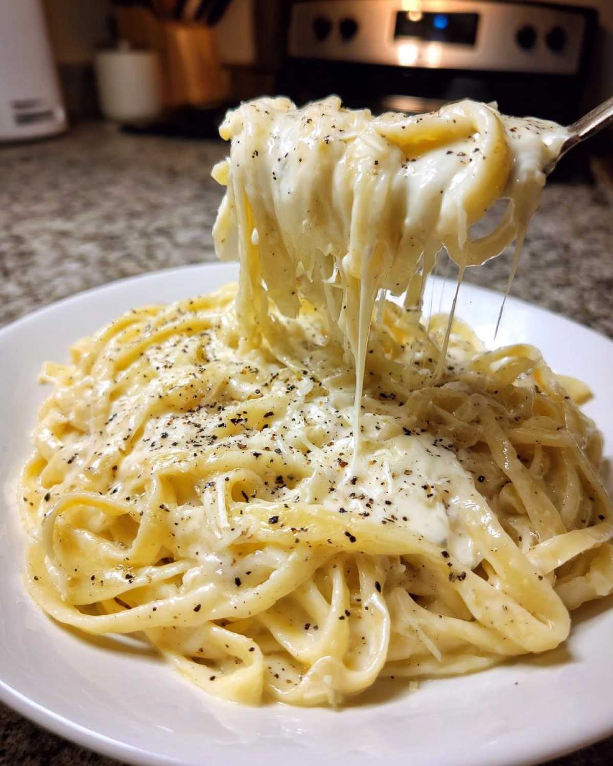 A fork lifts fettuccine noodles coated in creamy Olive Garden Alfredo Sauce, showing a cheese pull.