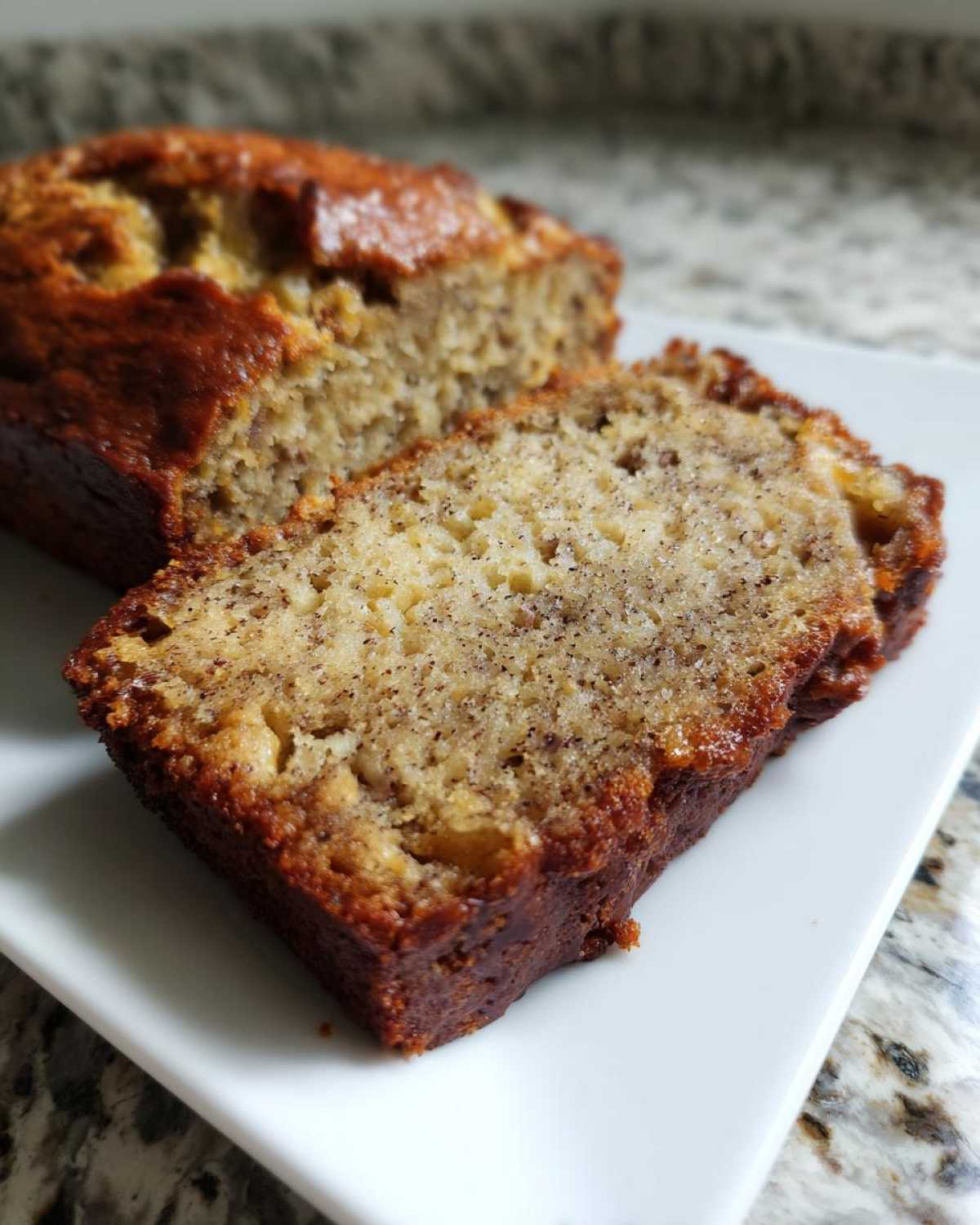 Close-up of a slice of moist sugar free banana bread next to the loaf on a white plate.