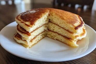 A tall stack of fluffy pancakes, cut to show the airy interior, drizzled with syrup.
