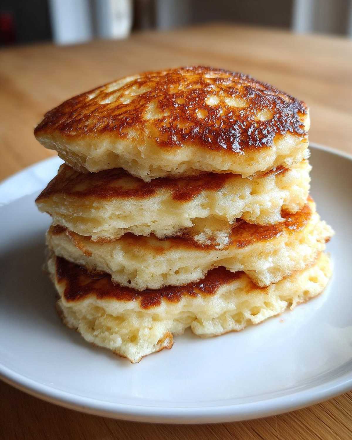 A tall stack of four golden brown, fluffy pancakes served on a white plate.