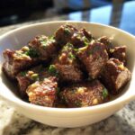 Close-up of tender, cubed crockpot steak bites glistening in sauce and topped with fresh green parsley.