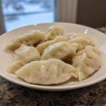 A white bowl filled with freshly steamed Traditional Chinese Dumplings sitting on a granite countertop.
