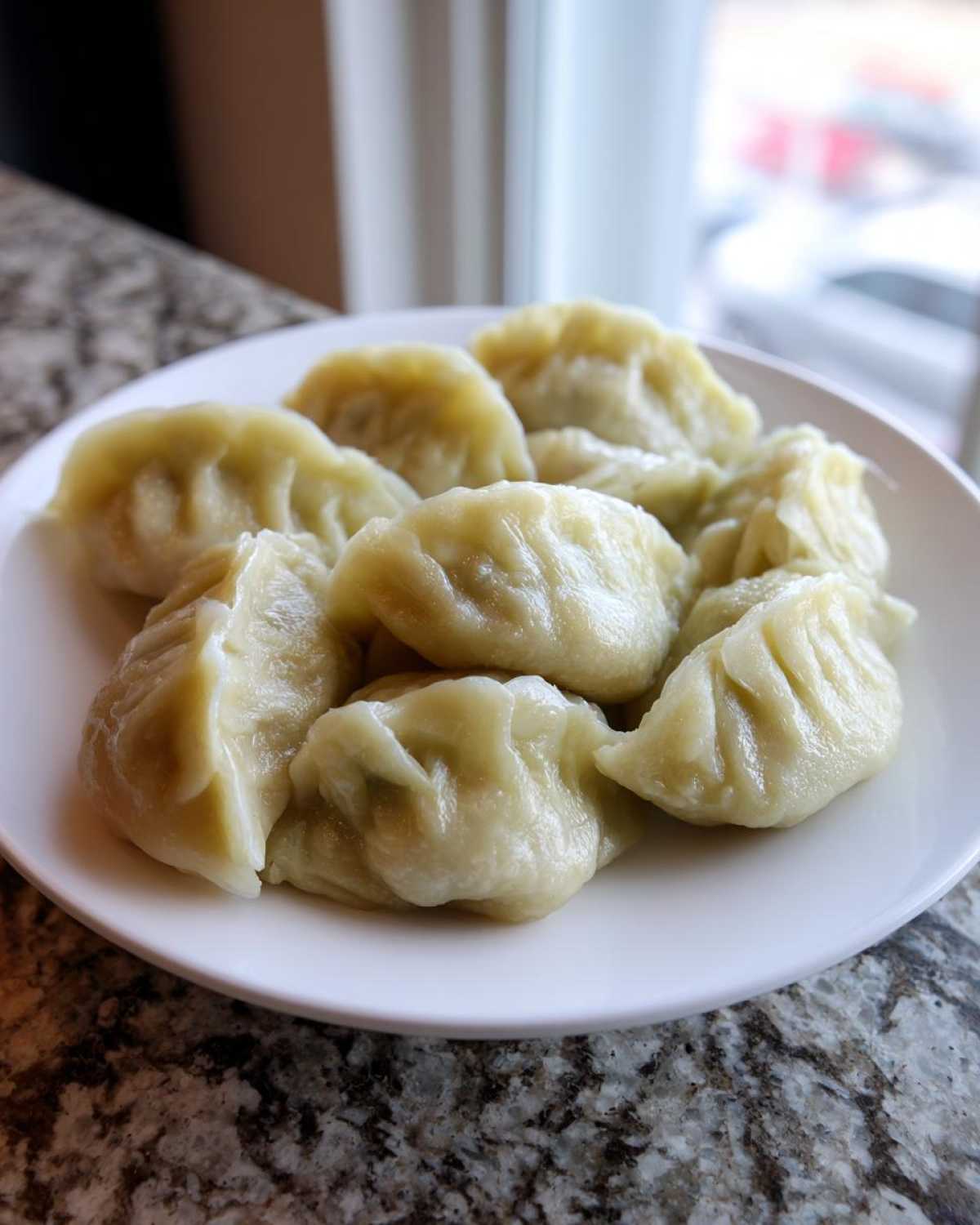 A white plate filled with freshly steamed Traditional Chinese Dumplings resting on a granite countertop.