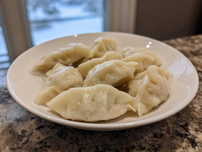 A white bowl filled with freshly steamed Traditional Chinese Dumplings sitting on a granite countertop.