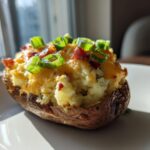 A close-up of a perfectly twice baked potato, stuffed with creamy filling, melted cheddar cheese, bacon bits, and topped with fresh green onions.