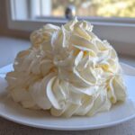 A large mound of perfectly piped, creamy vanilla buttercream frosting swirls on a white plate.