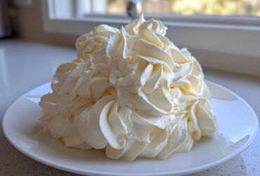 A large mound of perfectly piped, creamy vanilla buttercream frosting swirls on a white plate.