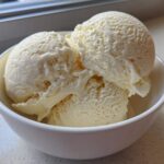 Three scoops of creamy, pale yellow protein ice cream served in a small white bowl.