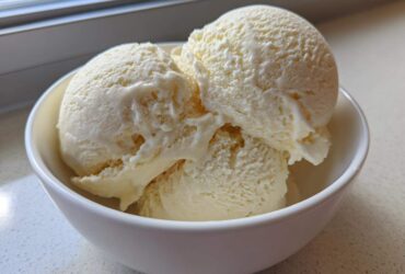 Three scoops of creamy, pale yellow protein ice cream served in a small white bowl.