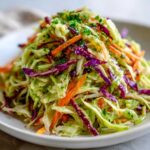 A close-up of a vibrant cabbage salad featuring shredded green and purple cabbage, carrots, and fresh parsley topping.