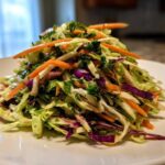 A mound of fresh, colorful cabbage salad featuring shredded green and purple cabbage, bright orange carrots, and green herbs.