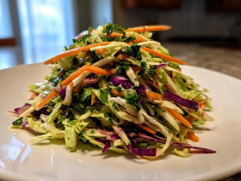 A mound of fresh, colorful cabbage salad featuring shredded green and purple cabbage, bright orange carrots, and green herbs.