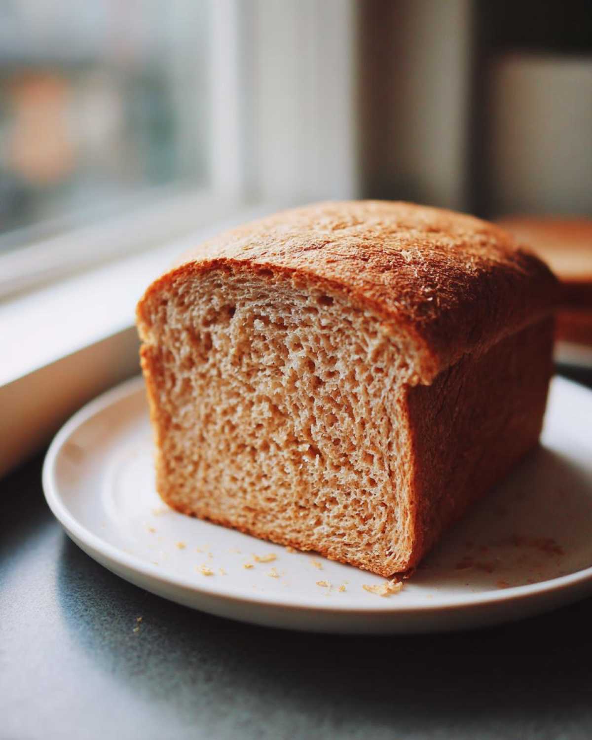 A freshly baked loaf of whole wheat bread, sliced to show the soft interior texture, resting on a white plate.