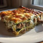 A thick, layered slice of zucchini lasagna with browned cheese topping sits on a white plate.