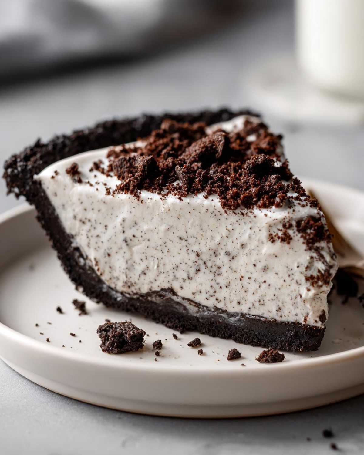 A close-up of a creamy slice of oreo pie with a dark chocolate crust and crushed cookie topping.