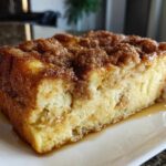 A close-up of a square slice of moist baked french toast topped with cinnamon streusel and syrup.