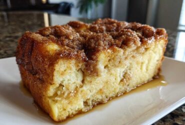 A close-up of a square slice of moist baked french toast topped with cinnamon streusel and syrup.