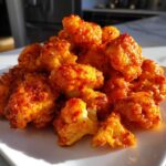A close-up pile of crispy, bright orange buffalo cauliflower bites served on a white plate.