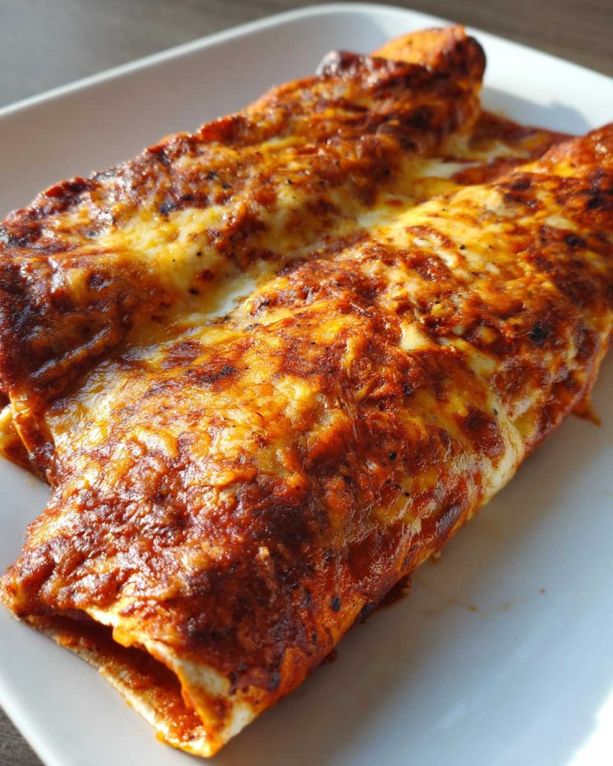 Close-up of two baked cheese enchiladas covered in bubbling red sauce and melted, browned cheese.