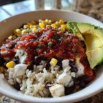 Close-up of a vibrant chicken burrito bowl featuring rice, black beans, corn, salsa, sour cream, and avocado slices.