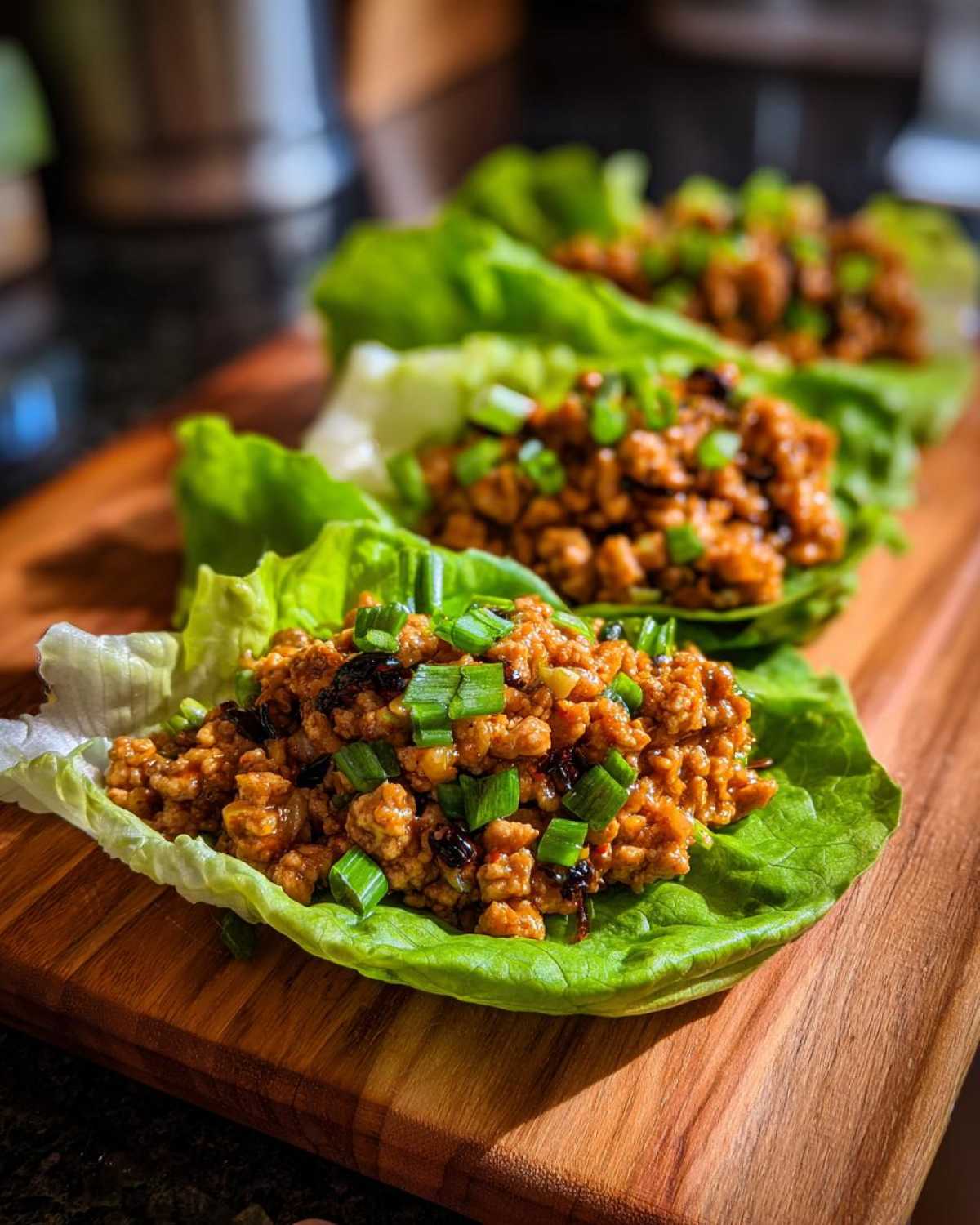 Three servings of flavorful chicken lettuce wraps, filled with savory ground chicken and topped with chopped green onions.