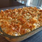 A freshly baked chicken noodle casserole in a clear glass dish, topped with golden cornflakes and parsley.