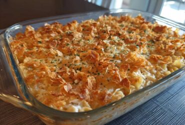 A freshly baked chicken noodle casserole in a clear glass dish, topped with golden cornflakes and parsley.