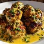 Close-up of several browned chicken piccata meatballs swimming in a bright lemon-butter sauce with capers and parsley.