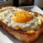 Close-up of a thick slice of golden brown egg toast topped with a sunny-side-up egg and cracked black pepper.