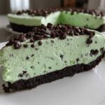 A close-up slice of creamy, mint-green grasshopper pie with a dark chocolate crust and chocolate chip topping.