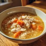 A close-up of a bowl of comforting turkey soup filled with shredded turkey, rice, and bright orange carrots.