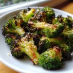 Close-up of bright green roasted broccoli florets topped with browned cheese, ready to eat.
