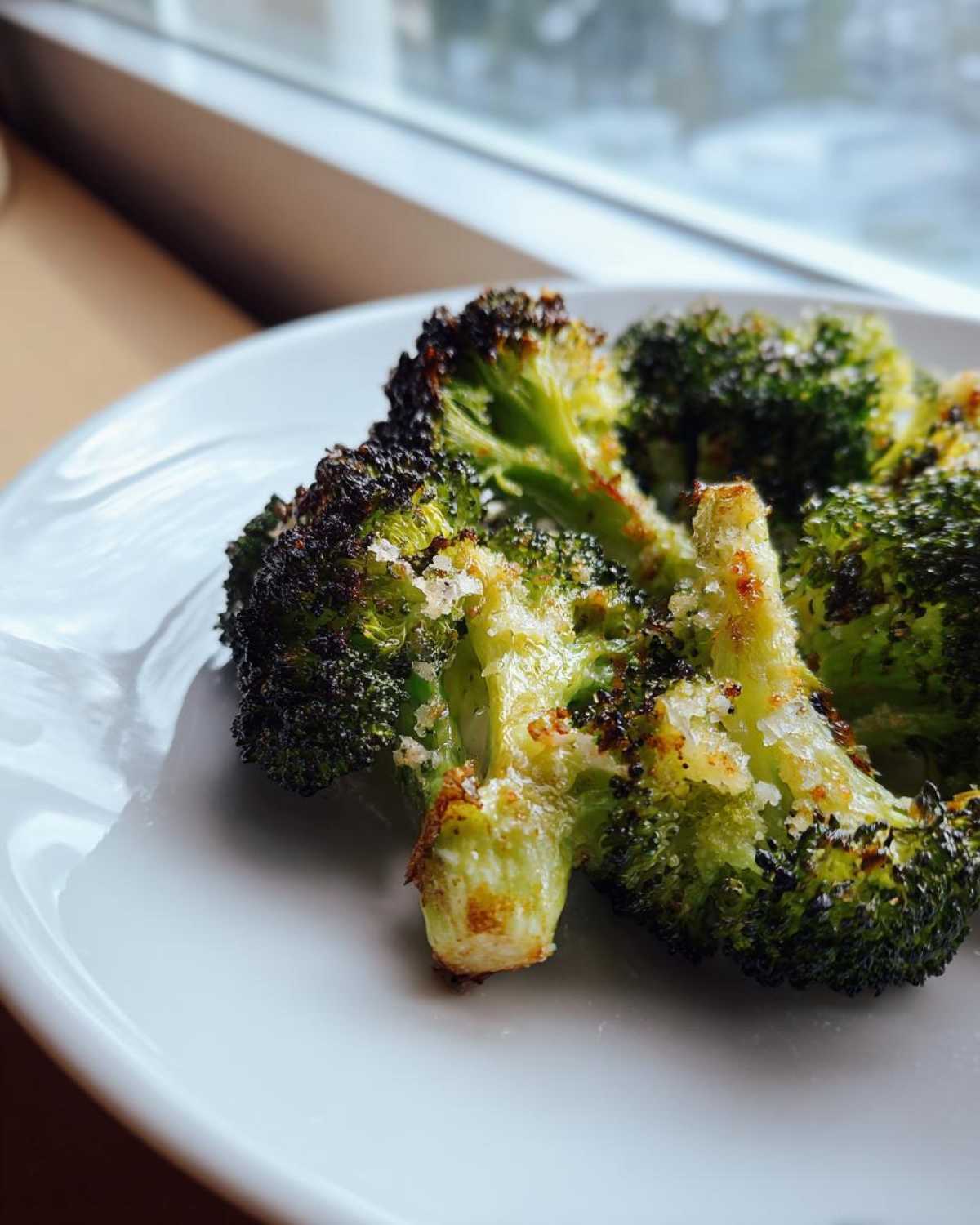 Close-up of perfectly roasted broccoli florets seasoned with coarse salt on a white plate.