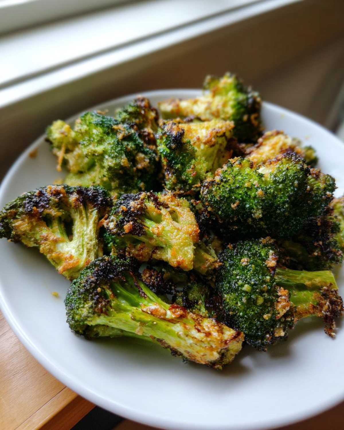 A close-up of perfectly seasoned and crispy roasted broccoli served on a white plate.