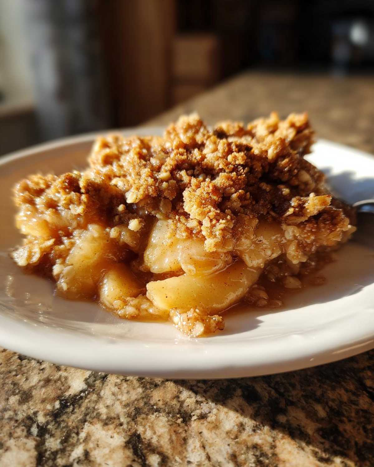 Close-up of a warm, golden slice of apple crisp recipe on a white plate, showing tender apples and crunchy topping.