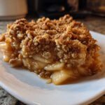 Close-up of a warm, gooey slice of apple crisp recipe showing tender apples and a thick, oat-based crumble topping.