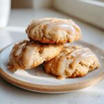 Three soft apple pie cookies stacked on a plate, generously drizzled with a caramel-colored glaze.