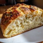 Close-up of the open crumb structure of freshly baked artisan bread topped with herbs.