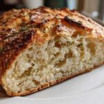 Close-up of a freshly baked artisan bread loaf, showing the open, airy crumb texture and rosemary topping.
