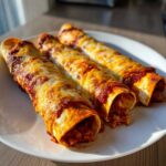 Three baked cheese enchiladas covered in red sauce and melted golden cheese, served on a white plate.