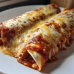 Close-up of two baked cheese enchiladas smothered in red sauce and melted white cheese.