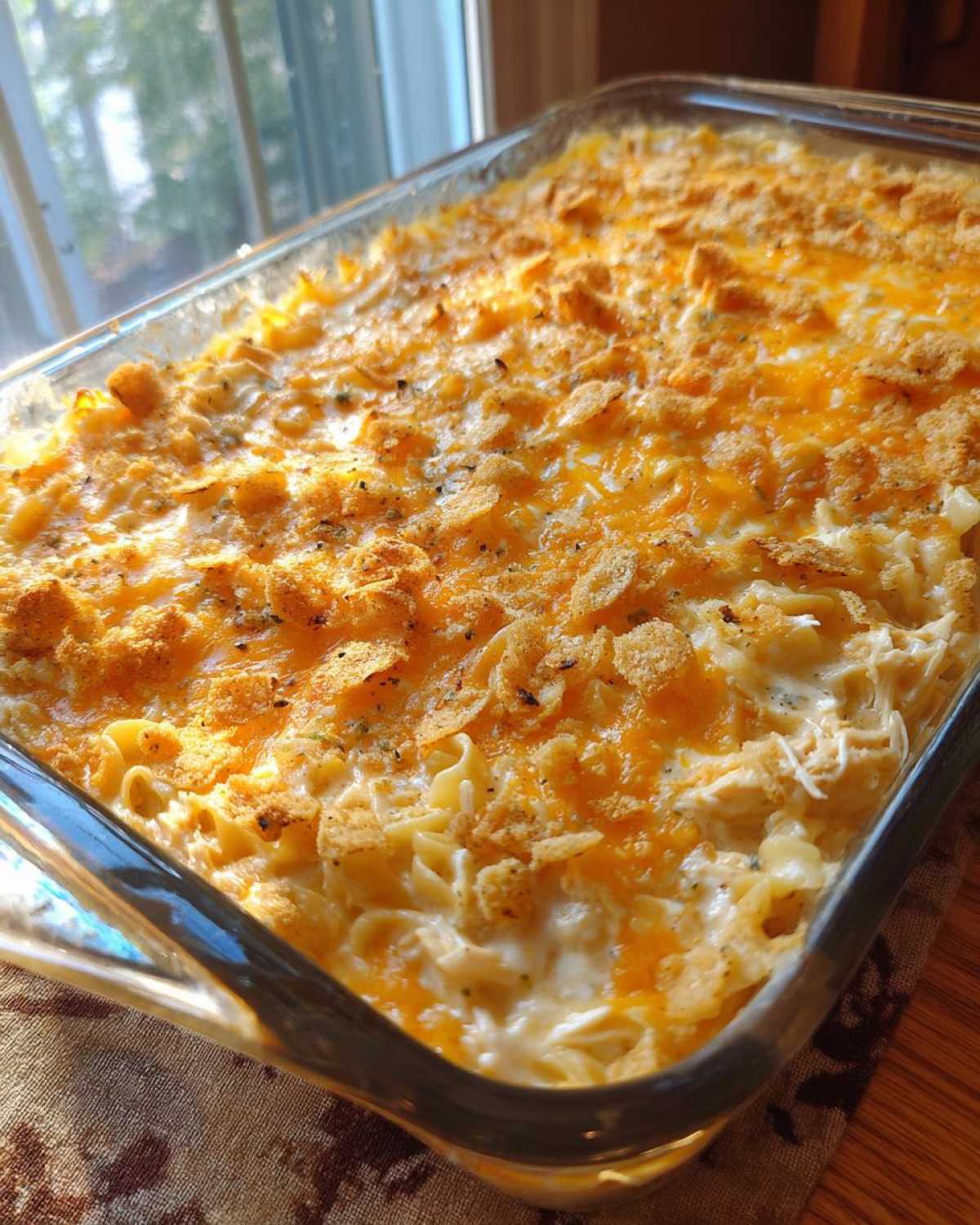 A freshly baked chicken noodle casserole in a glass dish, topped with melted cheddar cheese and crunchy breadcrumbs.