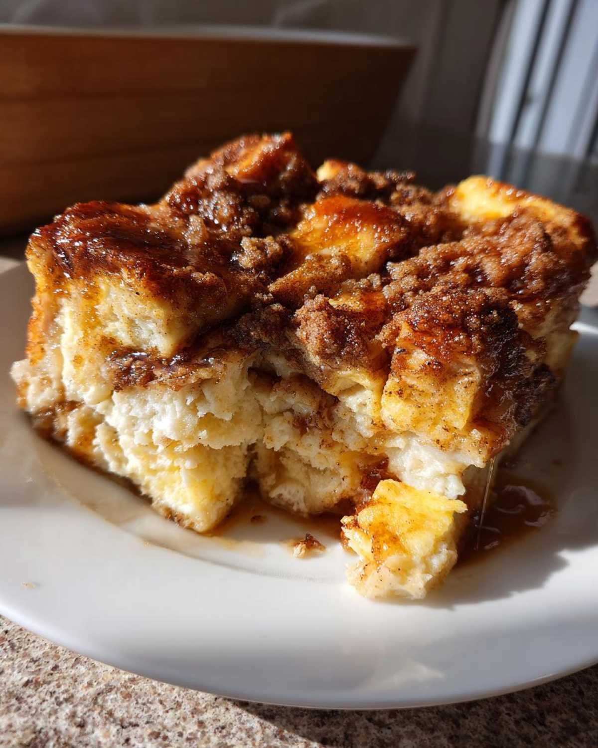 A close-up, sunlit serving of moist baked french toast casserole with a rich cinnamon-sugar topping.