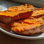 Close-up of bright orange baked sweet potato toast halves resting on a white plate in natural sunlight.