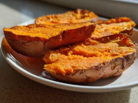 Close-up of bright orange baked sweet potato toast halves resting on a white plate in natural sunlight.