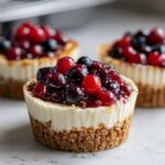 A close-up of a single berry topped mini cheesecake with a graham cracker crust and creamy filling.