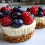 Close-up of two delicious mini cheesecake treats topped generously with fresh raspberries and blueberries.