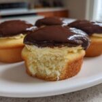 A close-up of delicious boston cream pie cupcakes showing the vanilla cake, pastry cream filling, and chocolate ganache topping.